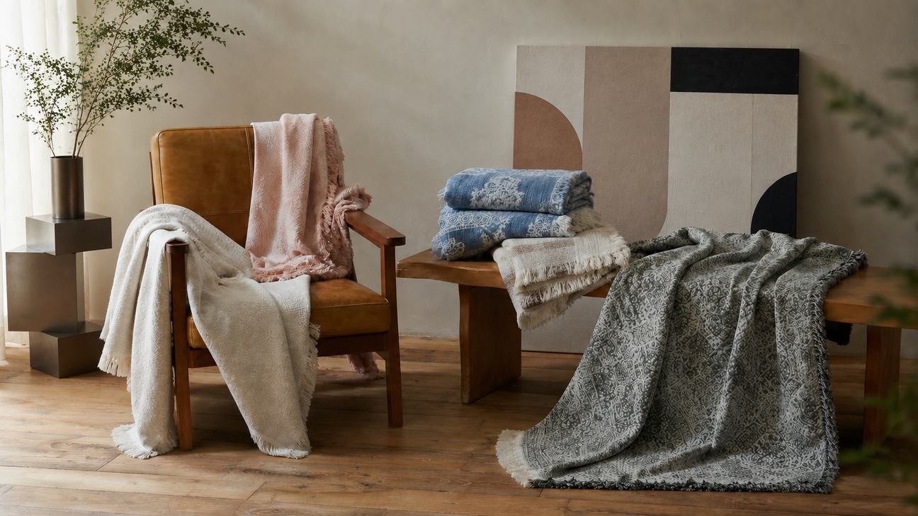 Collection of cotton-linen jacquard throw blankets in dusty rose, blue, and slate grey styled on a leather chair and wooden bench.