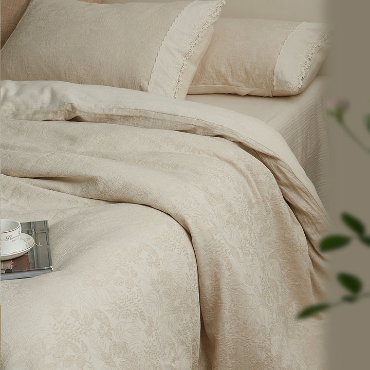 Angled bedroom view of the beige jacquard duvet cover and matching lace-trimmed pillow shams.