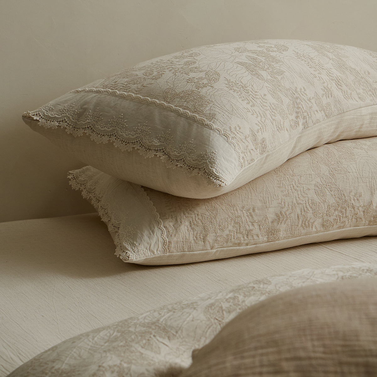 Close-up of stacked beige jacquard pillow shams with delicate lace edging and textured woven patterns.
