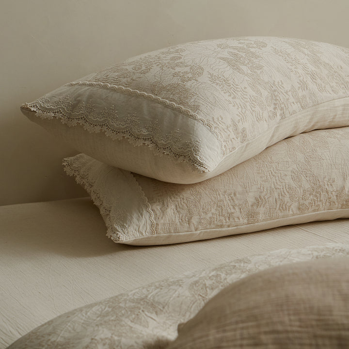 Close-up of stacked beige jacquard pillow shams with delicate lace edging and textured woven patterns.