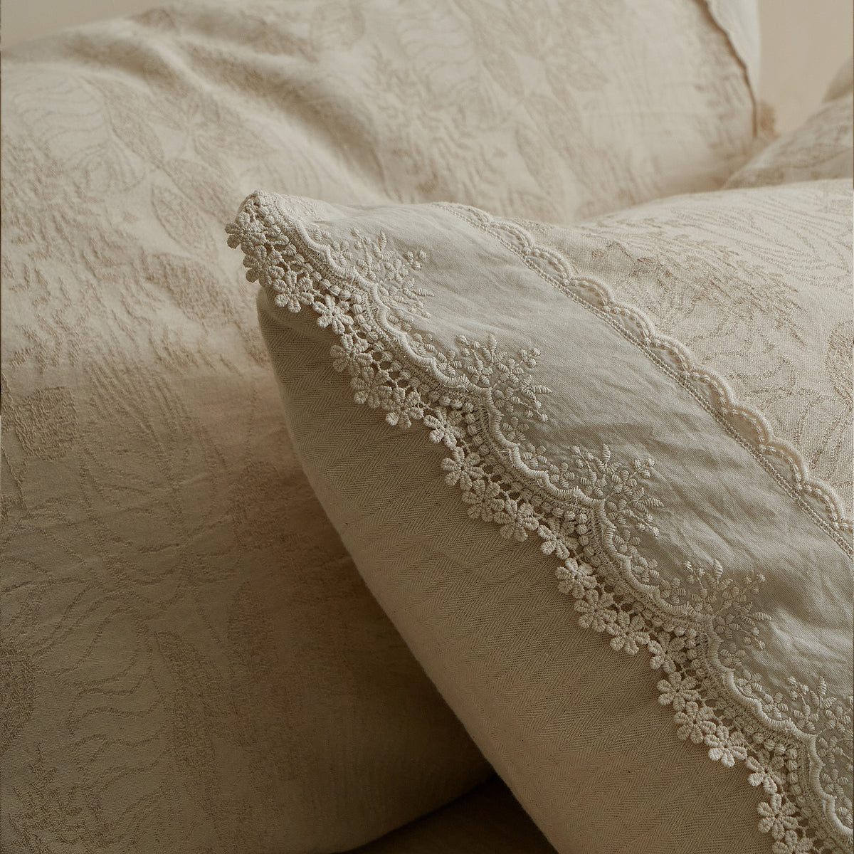 Detailed view of layered cotton-linen bedding with tonal jacquard patterns and delicate decorative edging.