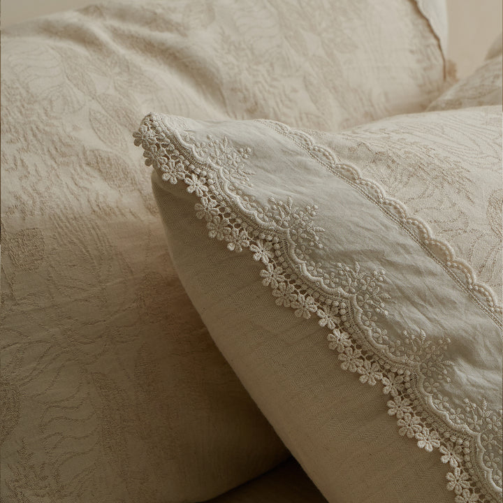 Detailed view of layered cotton-linen bedding with tonal jacquard patterns and delicate decorative edging.
