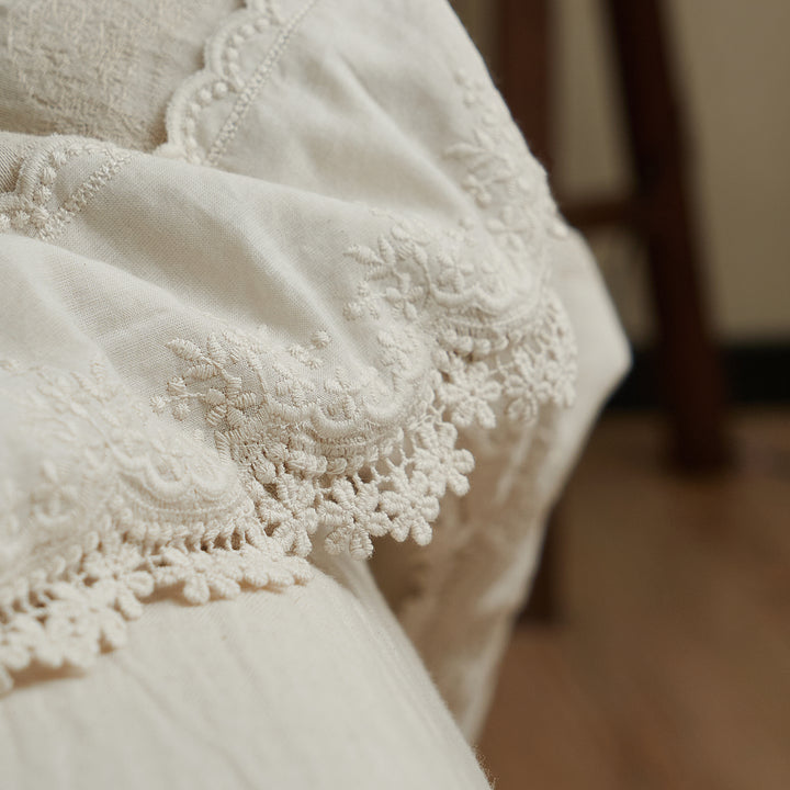 Detailed close-up of scalloped floral embroidery and delicate lace edging on beige cotton-linen bedding.