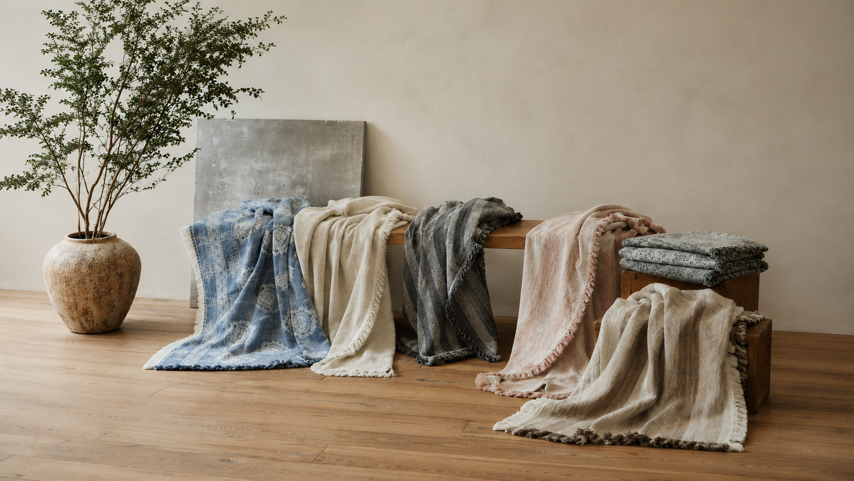 DAUAOTO collection of textured fringed throw blankets draped on a wooden bench in a minimalist wabi-sabi setting.