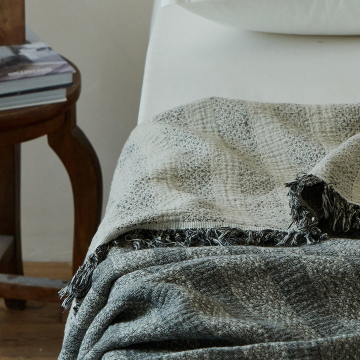 Charcoal black textured throw blanket draped elegantly, showing the striped fabric folds and fringe.