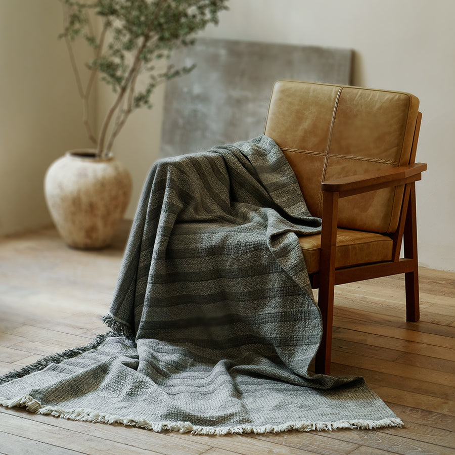 Charcoal black striped cotton-linen blanket draped casually over a brown leather armchair.