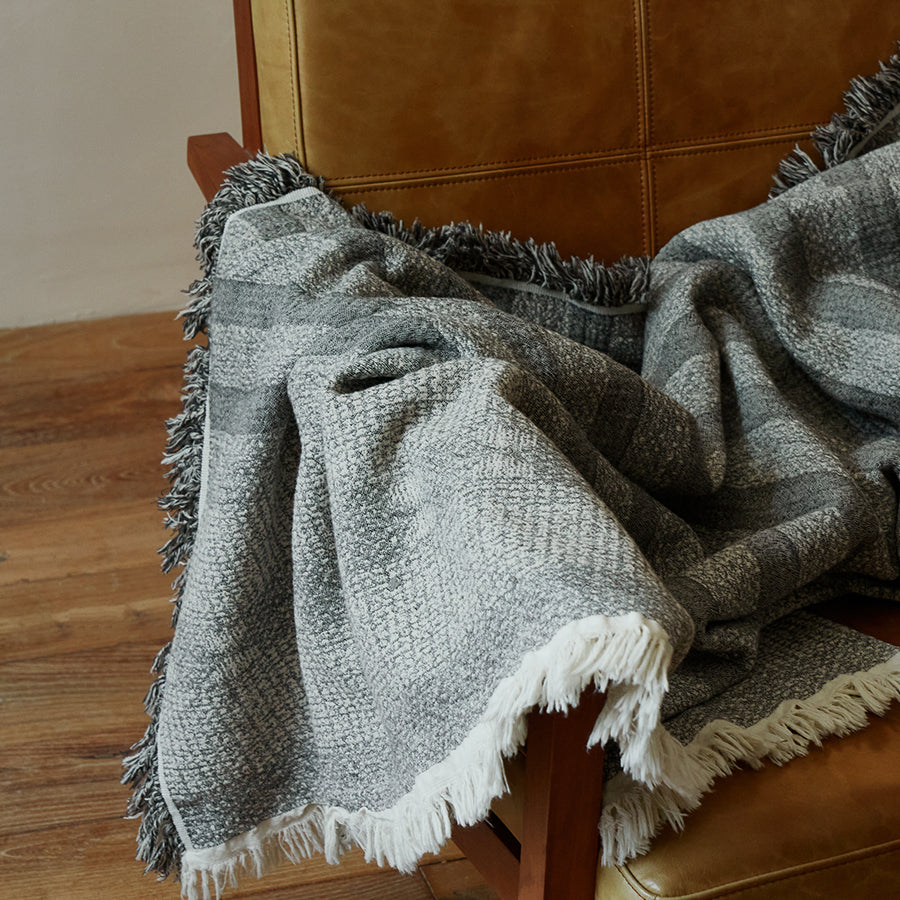 Charcoal black cotton-linen striped throw blanket gracefully draped over a reading chair.
