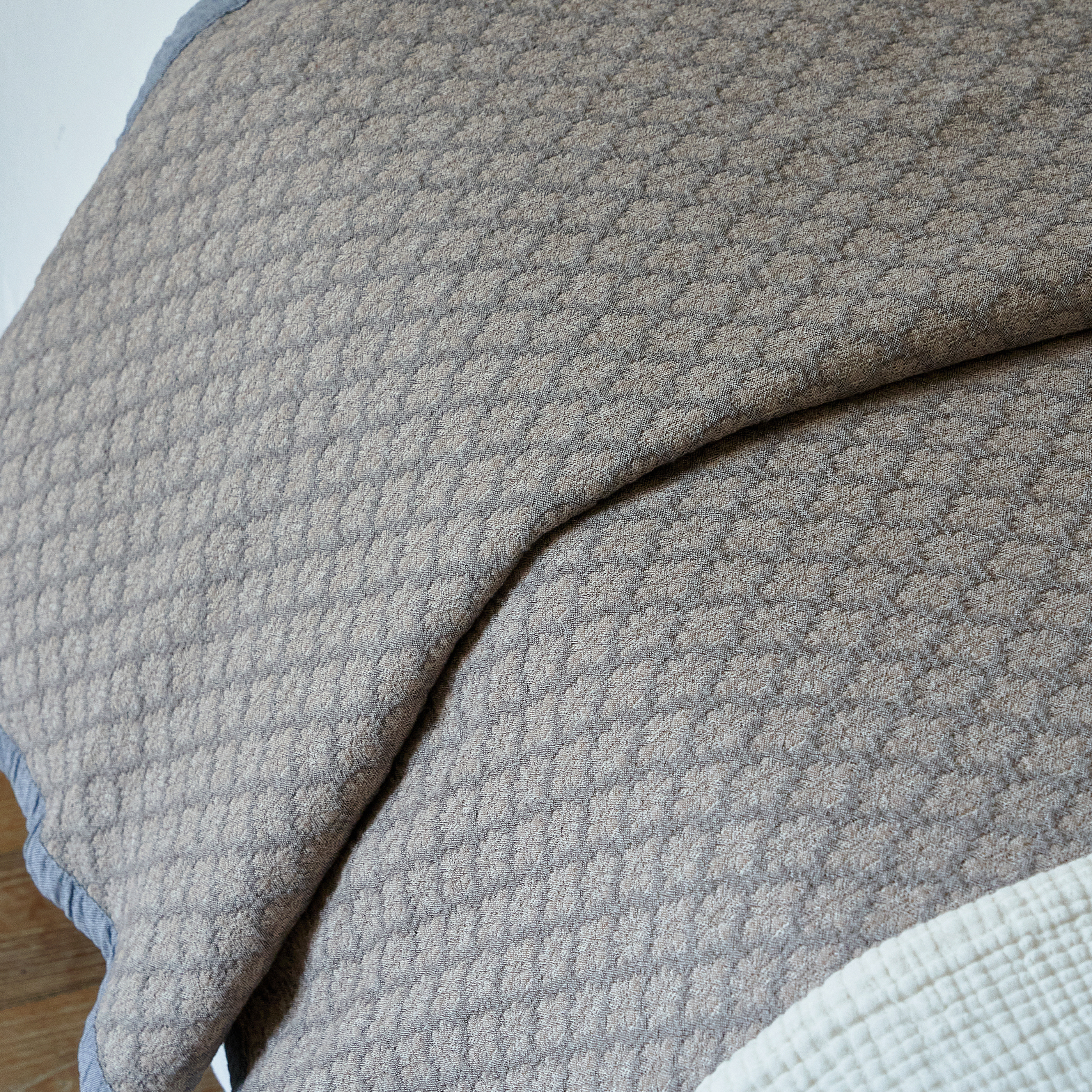 Folded edge of the charcoal gray jacquard coverlet revealing layered light bedding underneath.