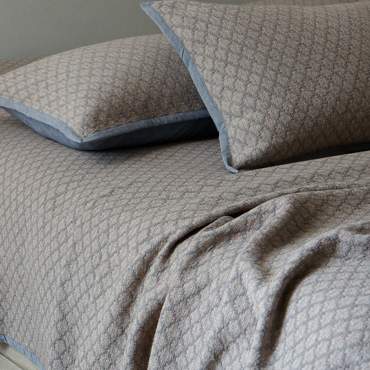 Charcoal gray diamond jacquard pillow sham resting on the matching textured coverlet.