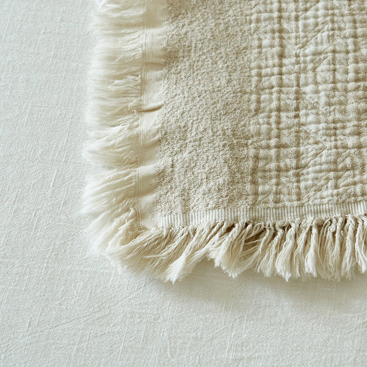 Macro shot of the intricate fringe detailing on the corner of the oatmeal cotton-linen blanket.