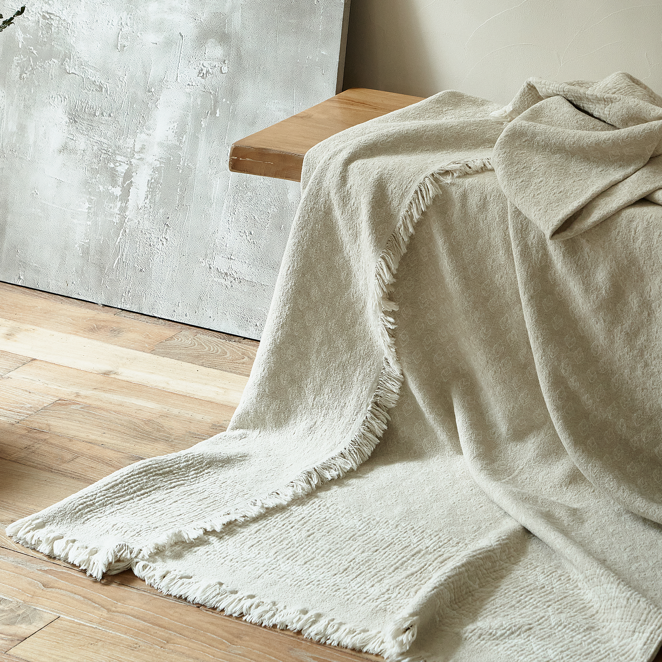 Oatmeal beige textured throw blanket draped over a bench, highlighting the natural drape and fringe edges.