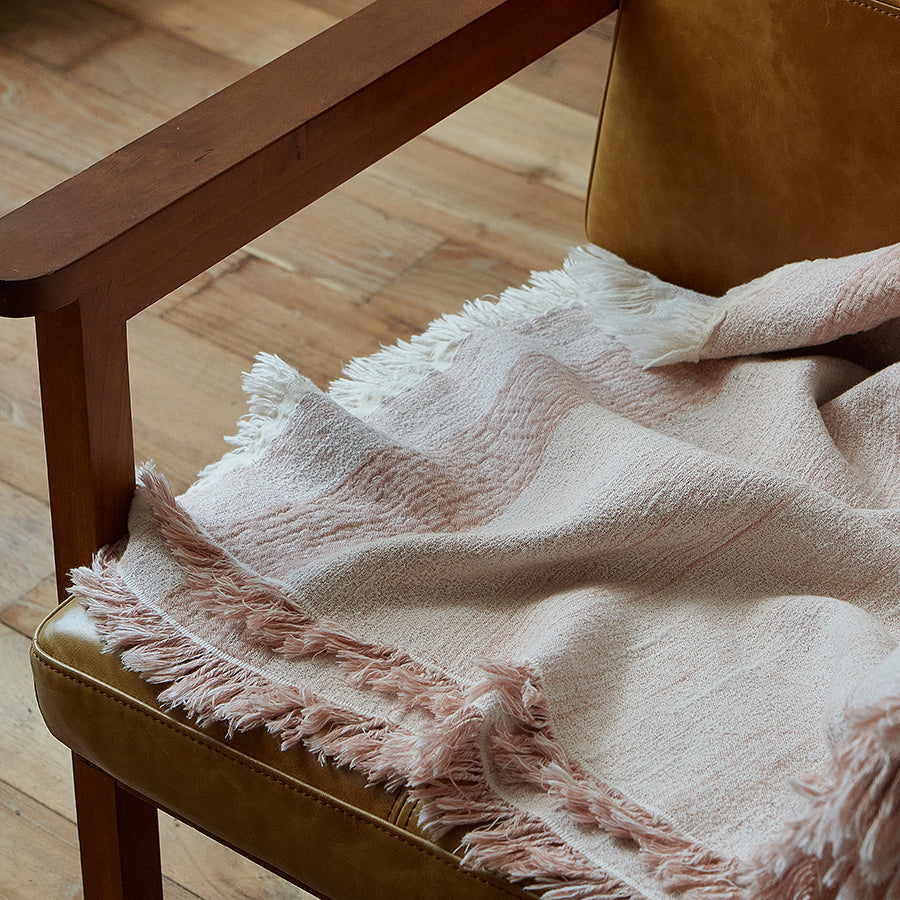 Close-up of the delicate fringe on the dusty rose cotton-linen throw resting on a chair arm.