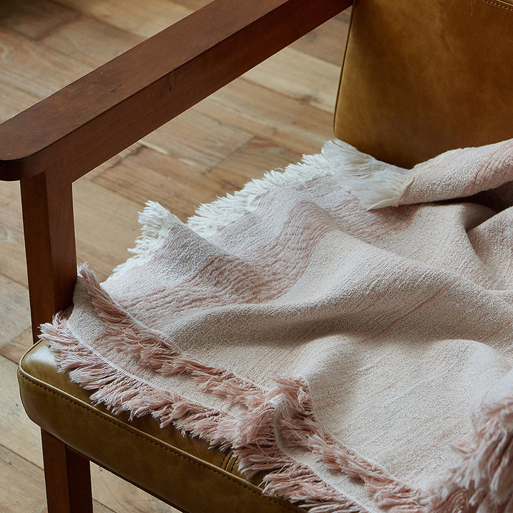 Close-up of the delicate fringe on the dusty rose cotton-linen throw resting on a chair arm.