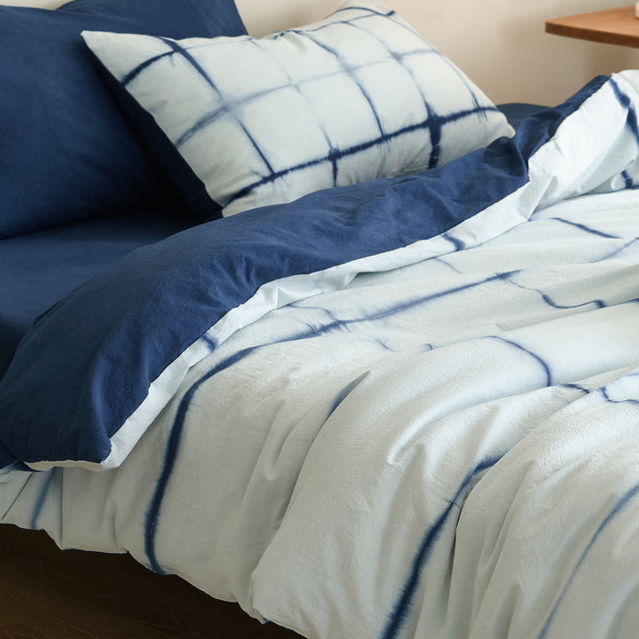 Folded DAUAOTO Artisan Grid duvet cover and pillowcase revealing the solid botanical indigo reverse side