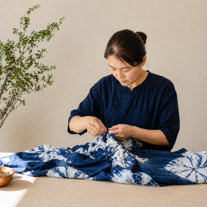 Female artisan meticulously hand-tying pure white cotton fabric for DAUAOTO's traditional botanical dyeing process.