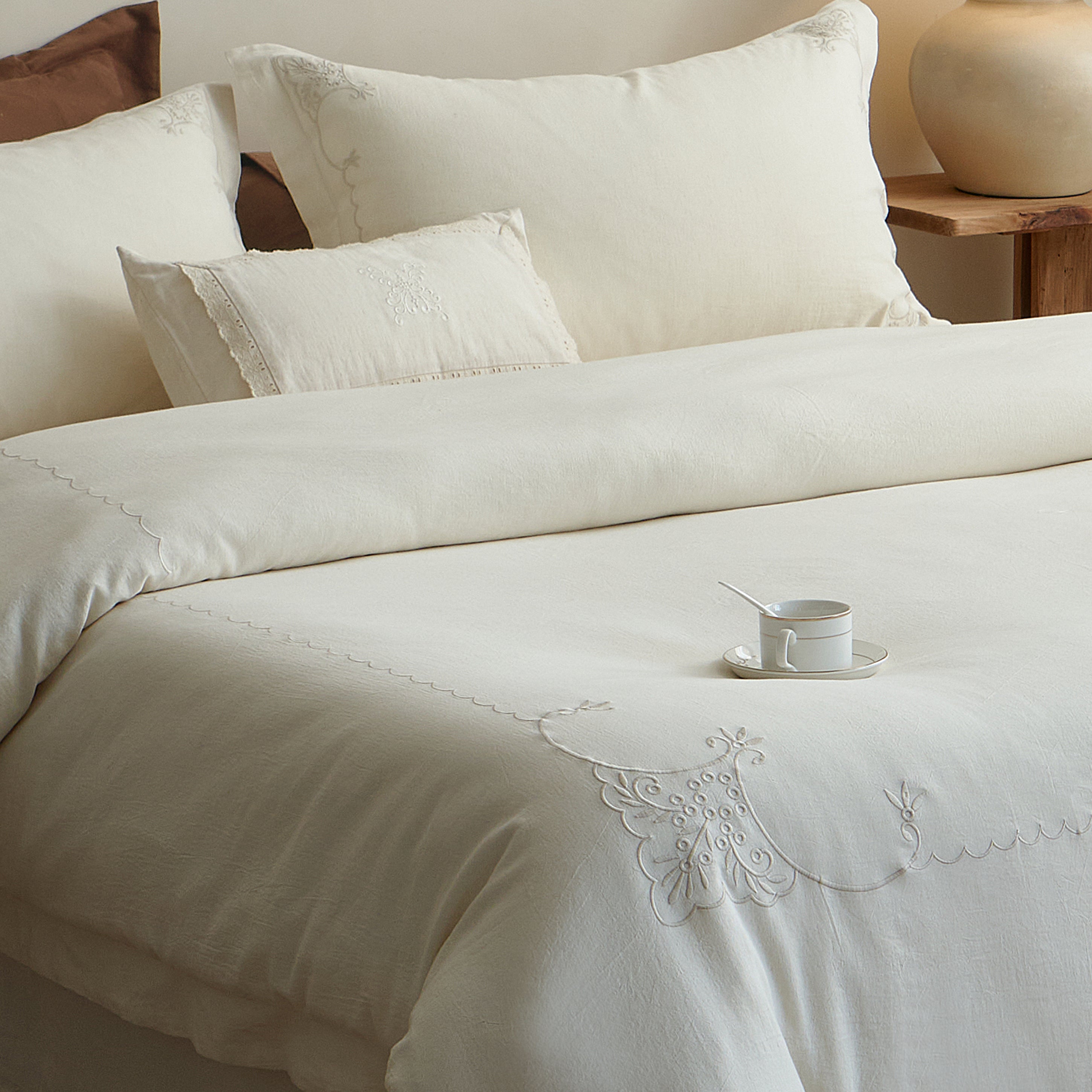 Angled view of the Aveline embroidered duvet cover set styled with natural ivory and muted brown pillows.