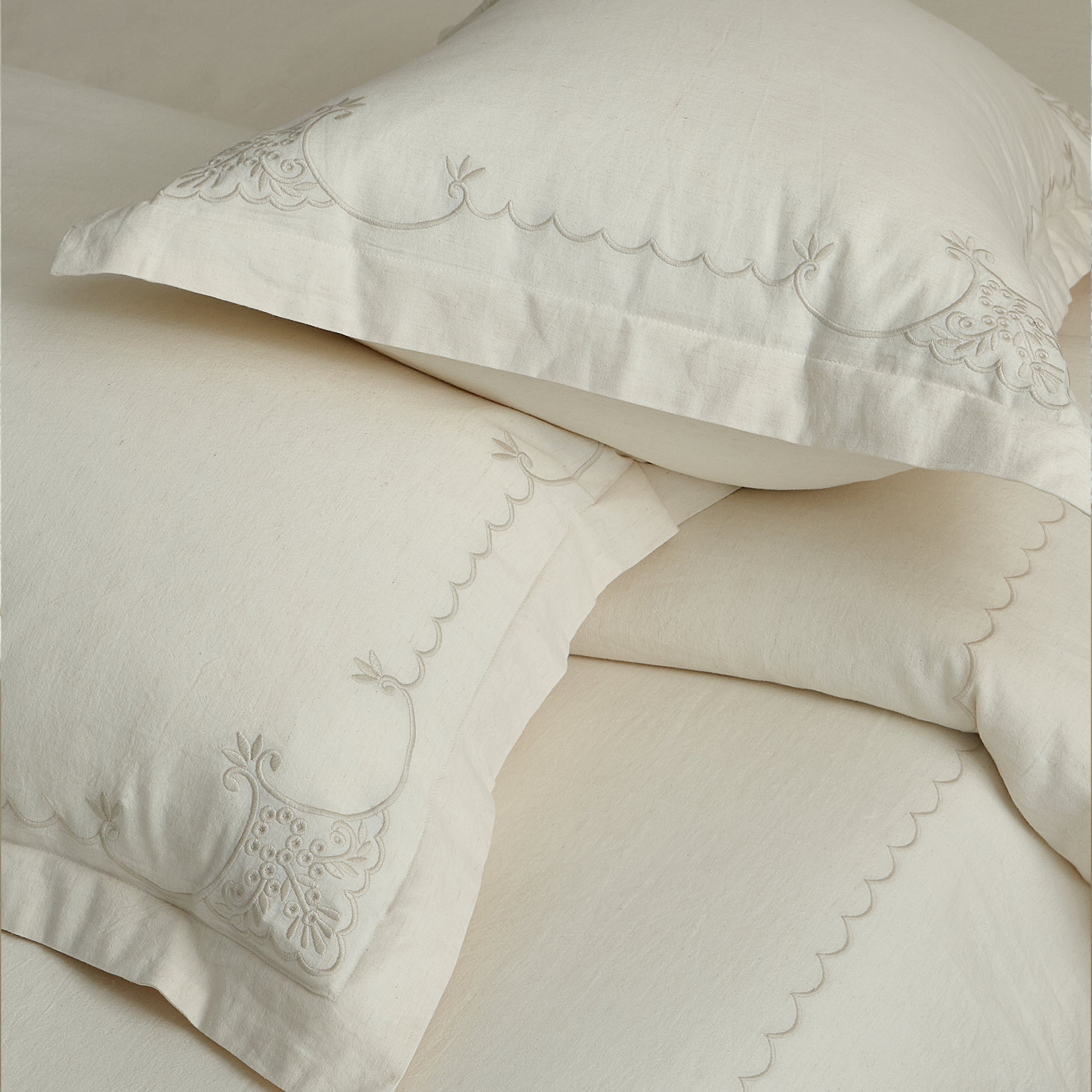 Layered Aveline pillow shams and duvet cover showing continuous scalloped embroidery along the edges.