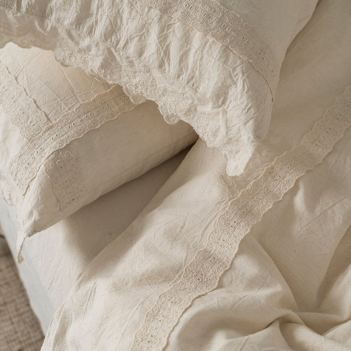 Close-up of the Fontainebleau cotton-linen duvet cover and pillow shams in natural ivory, featuring vintage embroidery and scalloped lace trim.