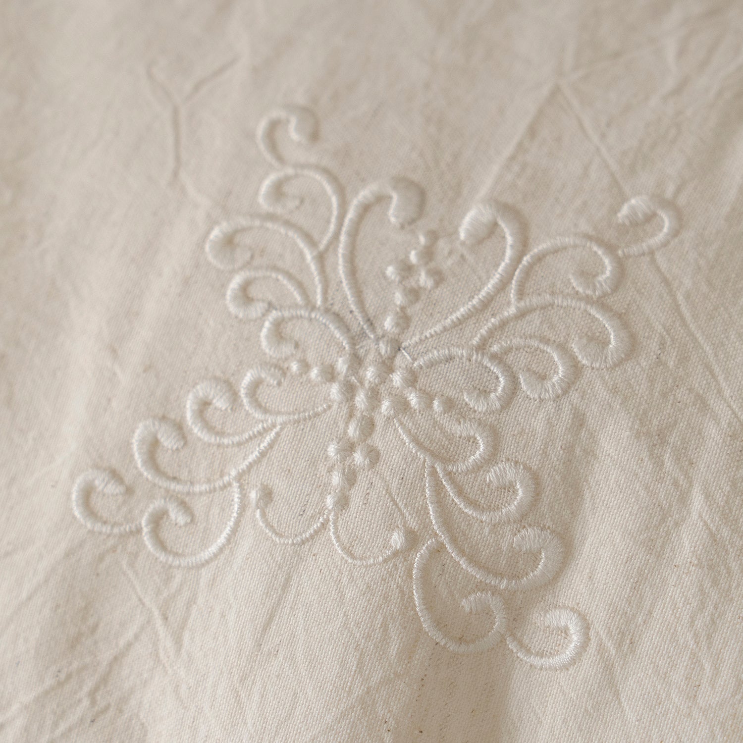 Macro close-up of the delicate vintage-inspired embroidery pattern on the Fontainebleau cotton linen fabric.