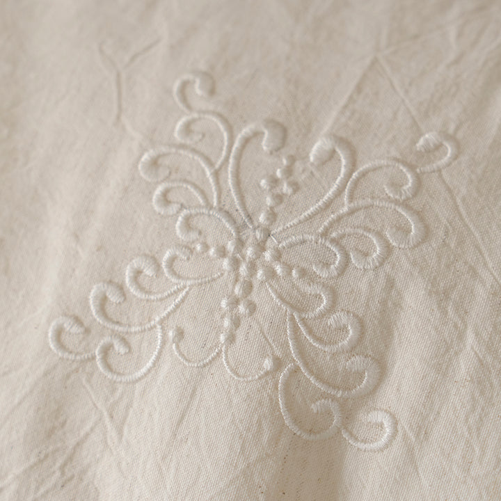 Macro close-up of the delicate vintage-inspired embroidery pattern on the Fontainebleau cotton linen fabric.