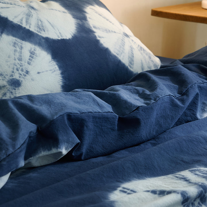 Soft folds of the DAUAOTO handmade botanical indigo tie-dye pillowcase resting naturally on a bed.