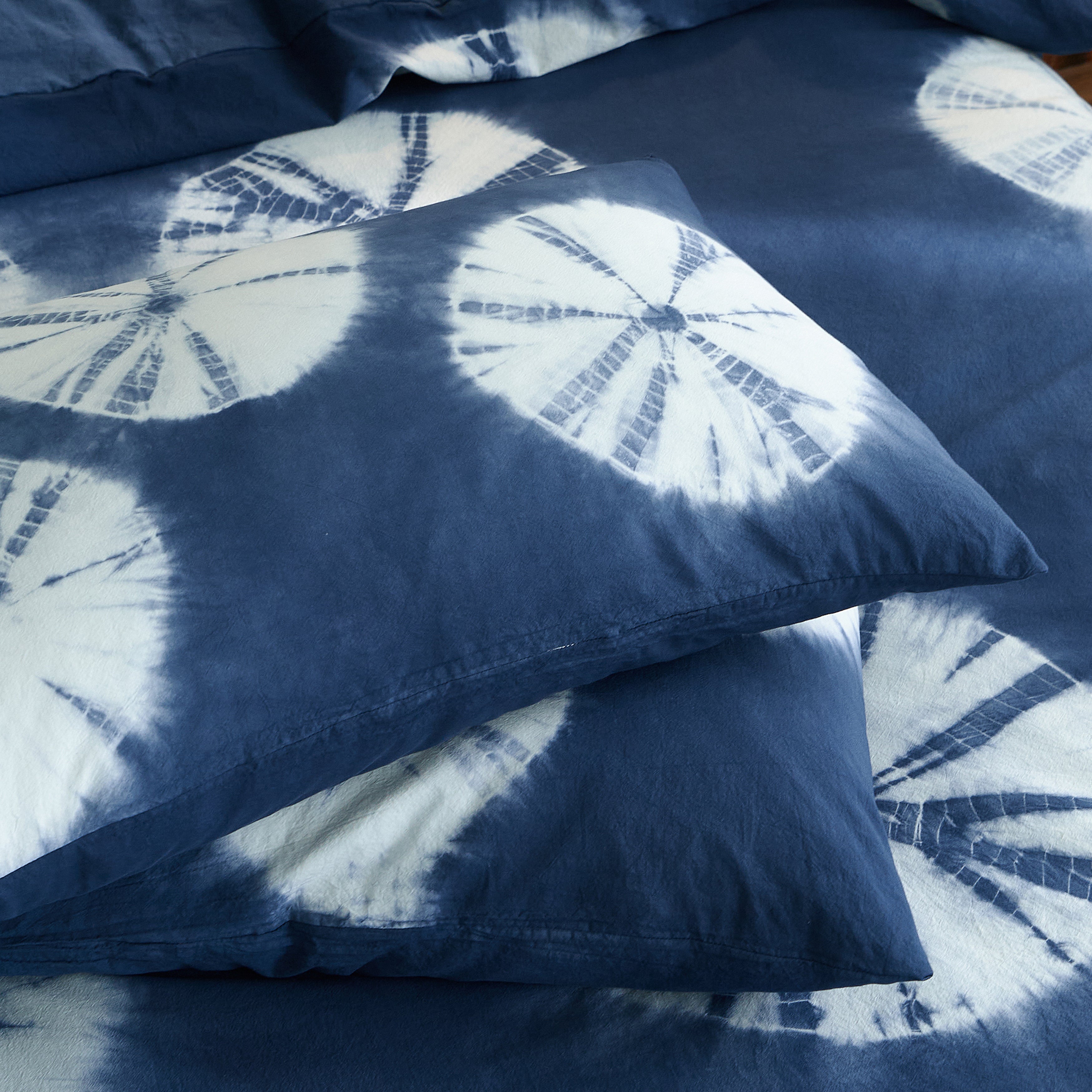 Two DAUAOTO Indigo Bloom 100% cotton pillowcases neatly stacked, showing bespoke tie-dye artistic patterns.