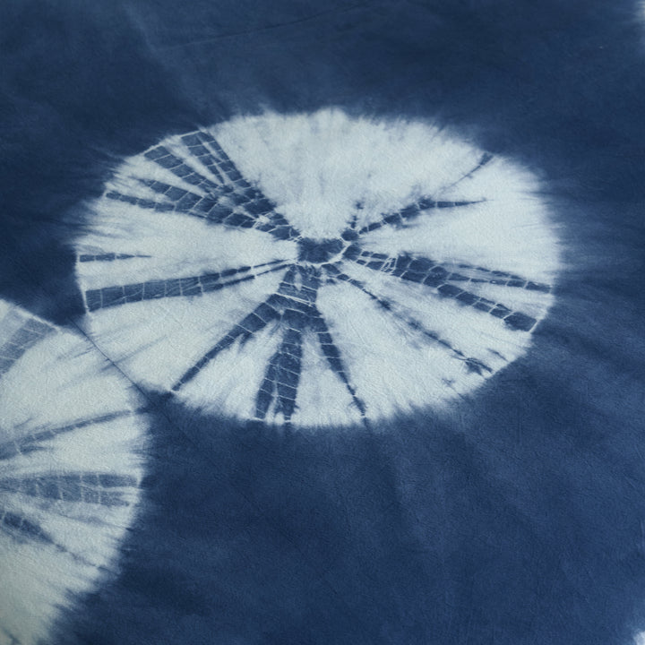 Macro shot of the unique hand-tied white circular sunburst pattern against deep botanical indigo pure cotton.