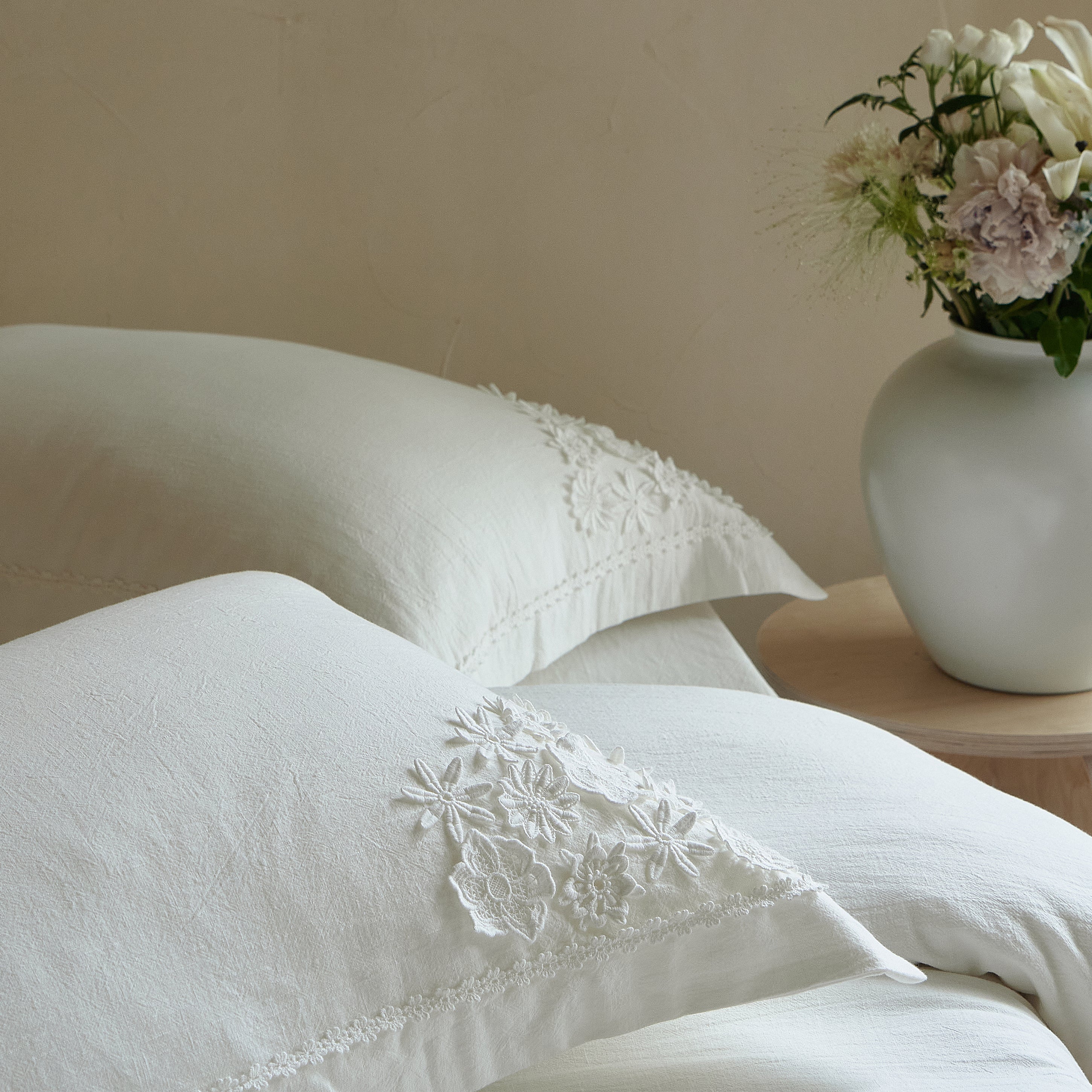 Morning Meadow embroidered pillow sham styled with textured white cotton bedding in a neutral bedroom.