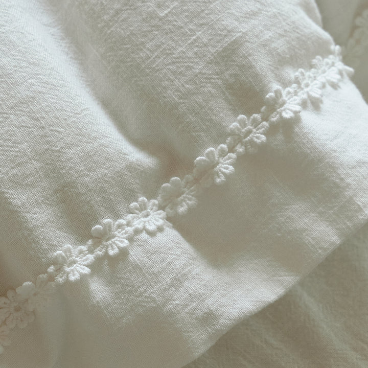 Close-up of delicate white floral trim stitched along the textured cotton duvet cover.