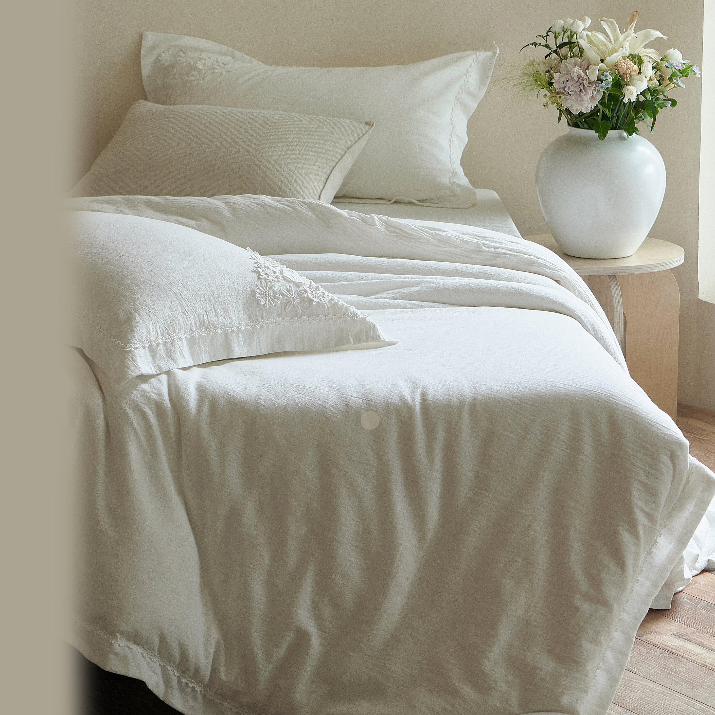 Side view of the Morning Meadow white bedding showing its relaxed drape, layered pillows, and floral trim.
