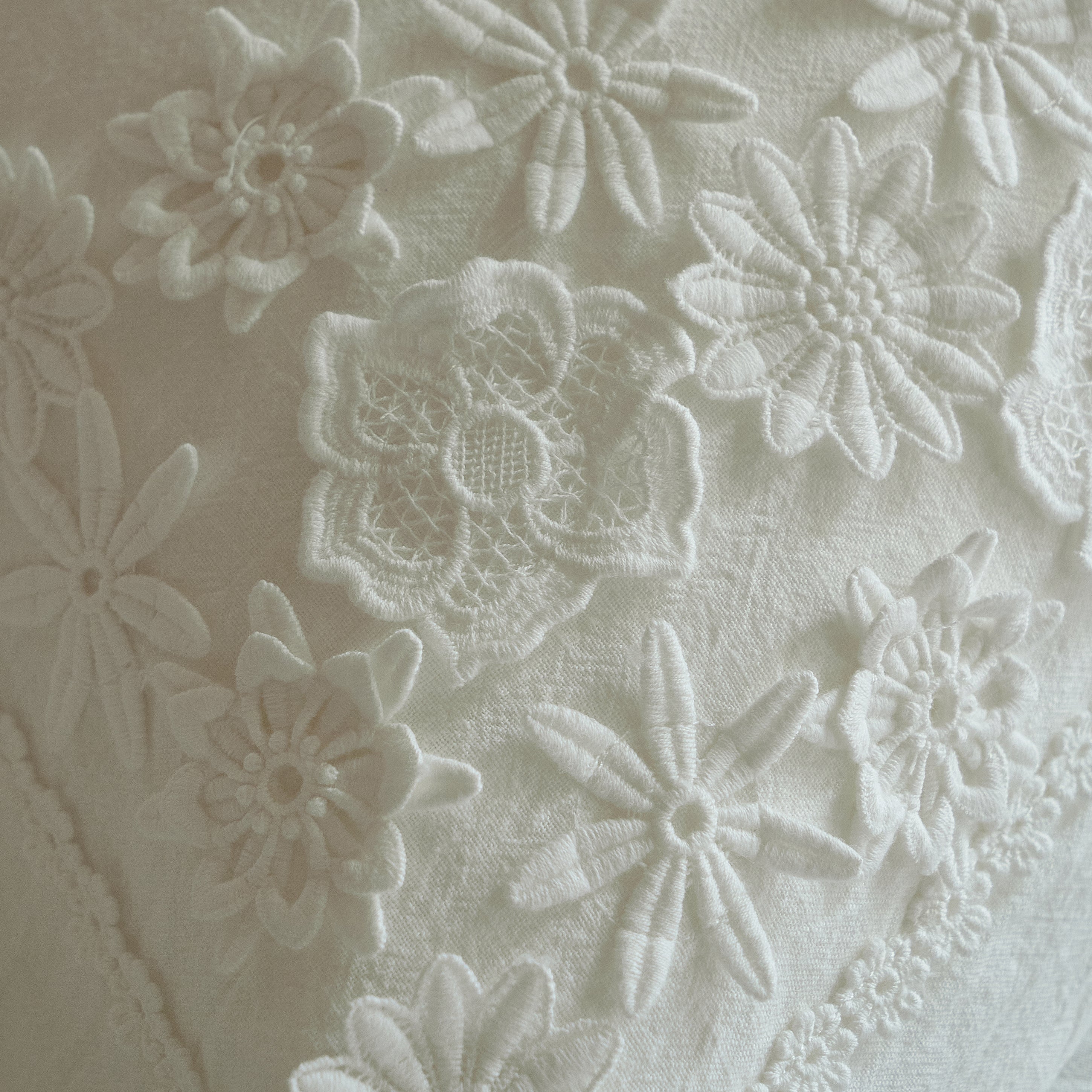 Close-up of raised white-on-white botanical embroidery and fine openwork on the Morning Meadow pillow sham.
