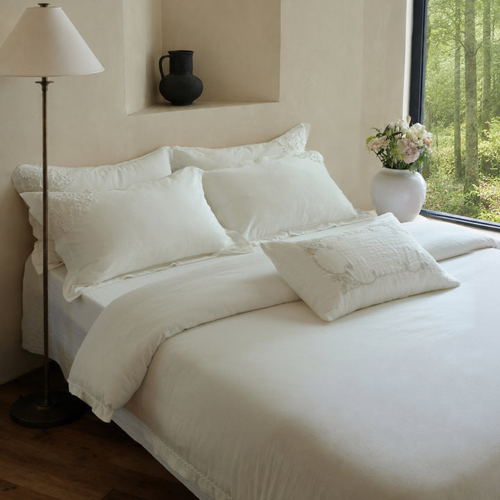 Angled bedroom view of the Morning Meadow white cotton duvet cover set with coordinating embroidered pillow shams.