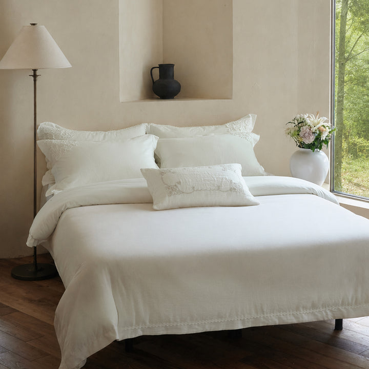 Front view of the Morning Meadow white embroidered cotton duvet cover set in a warm neutral bedroom.