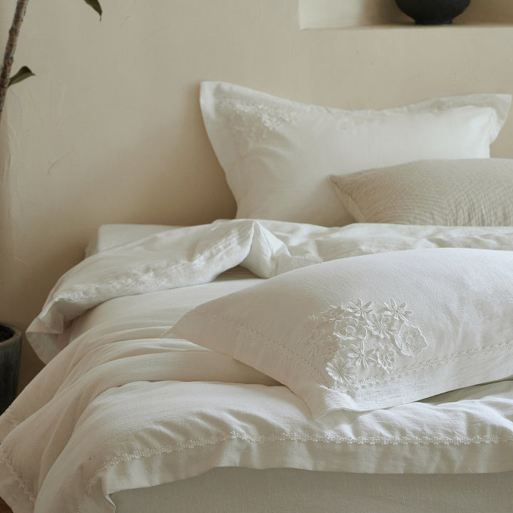 Morning Meadow white cotton duvet cover set styled in a warm neutral bedroom with botanical embroidery and delicate floral trim.
