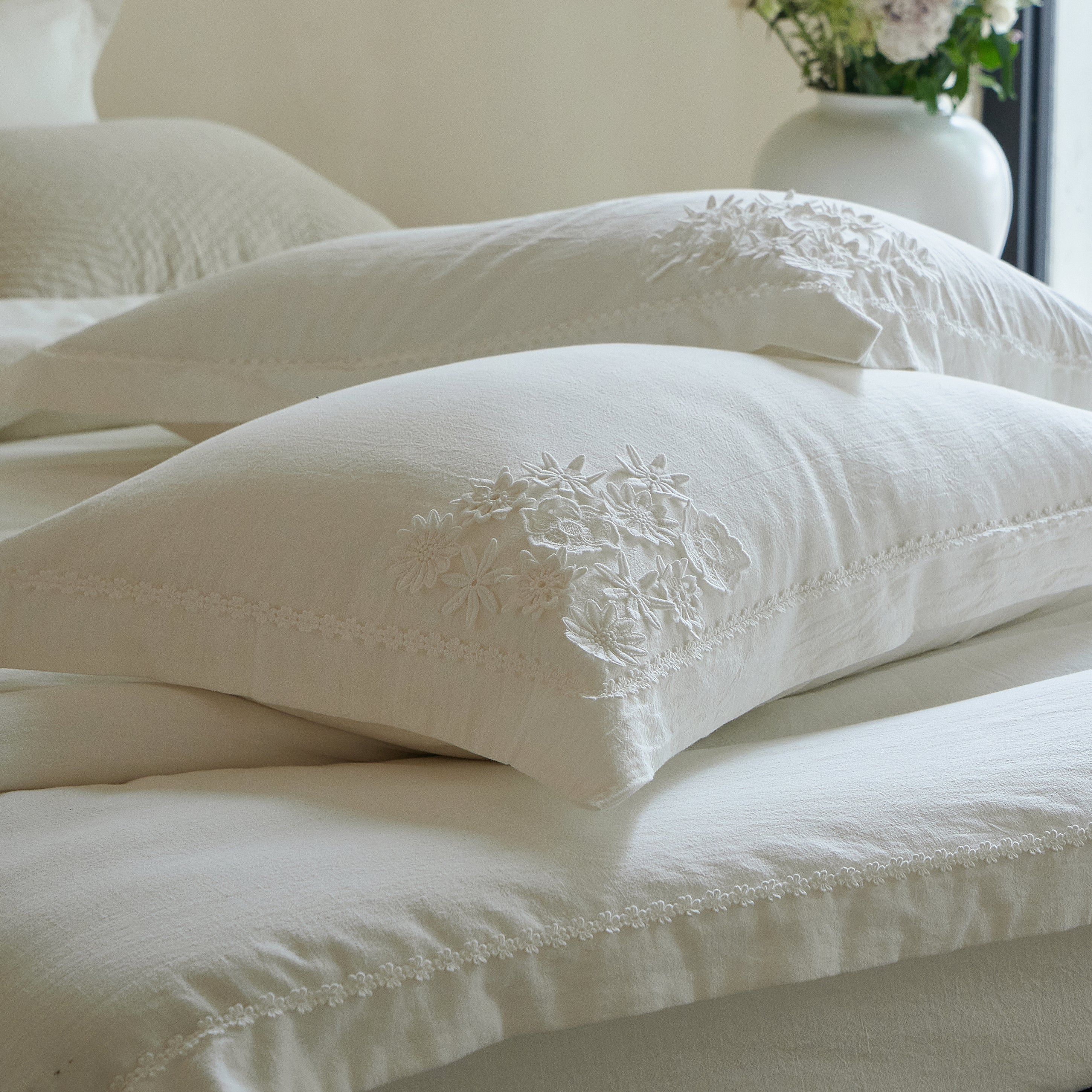 Close-up of the Morning Meadow white pillow sham featuring dimensional botanical embroidery and floral edge trim.