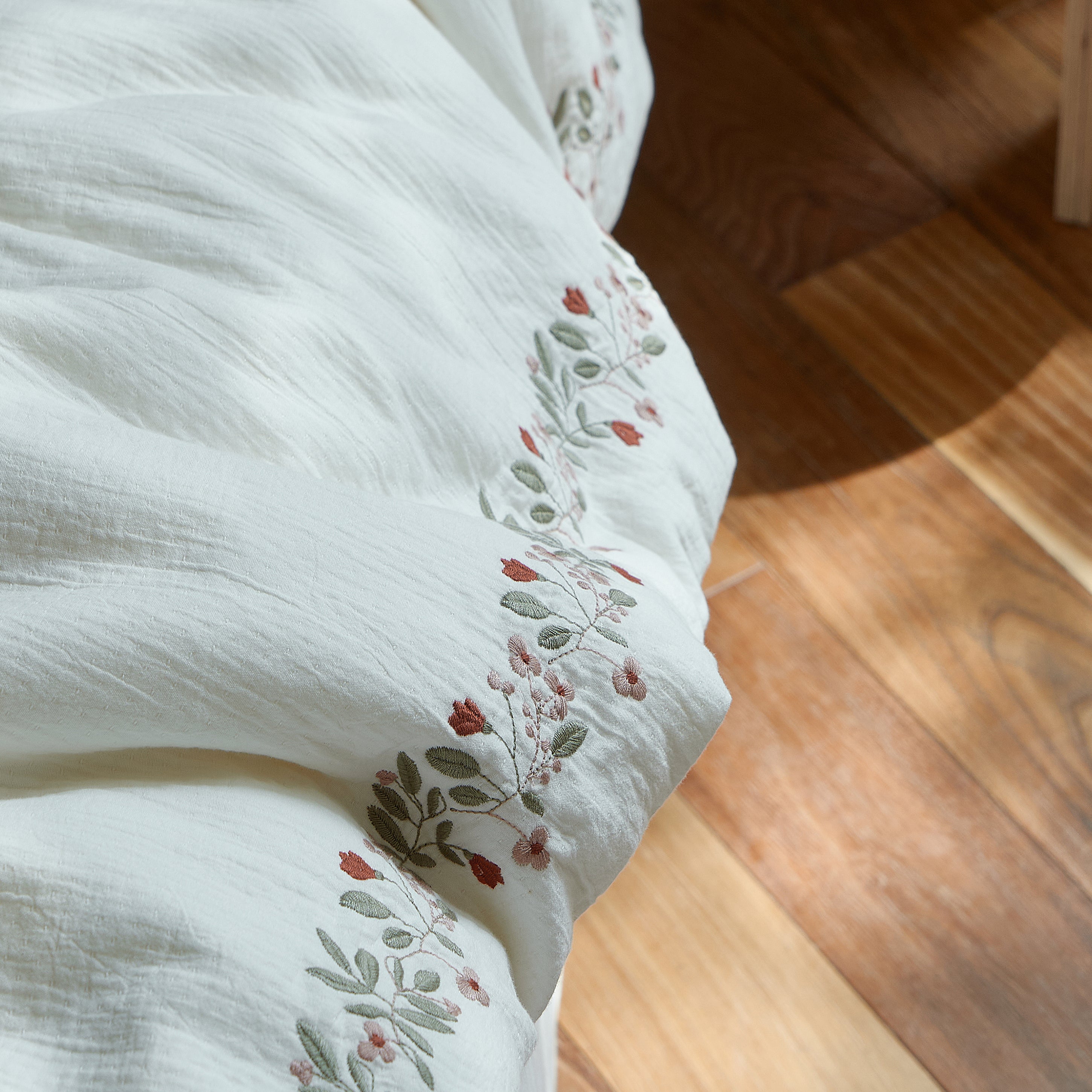 Close-up of the continuous floral embroidery along the edge of the Rosebud Garland duvet cover.