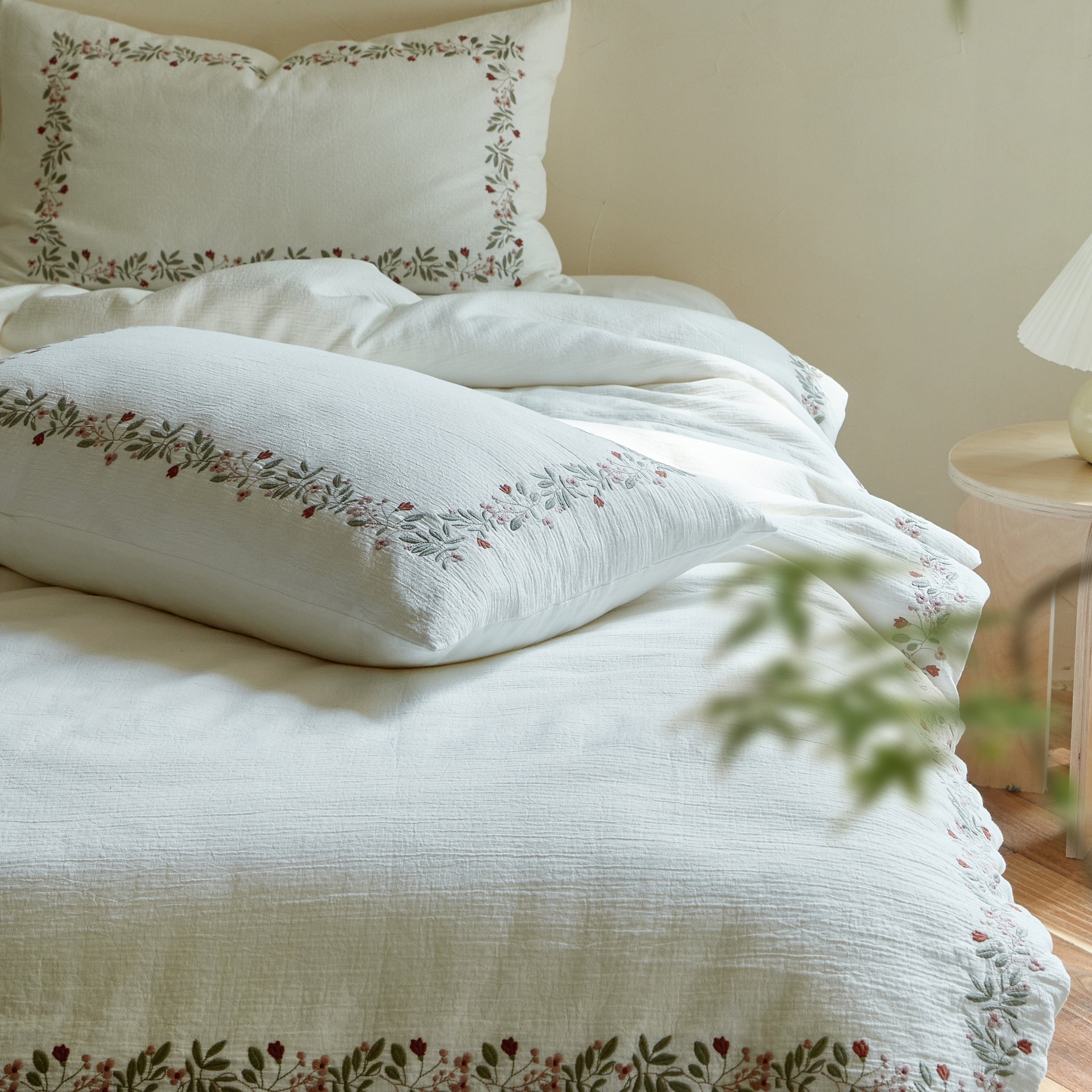 Rosebud Garland duvet cover and matching embroidered pillow shams arranged together on a white bed.