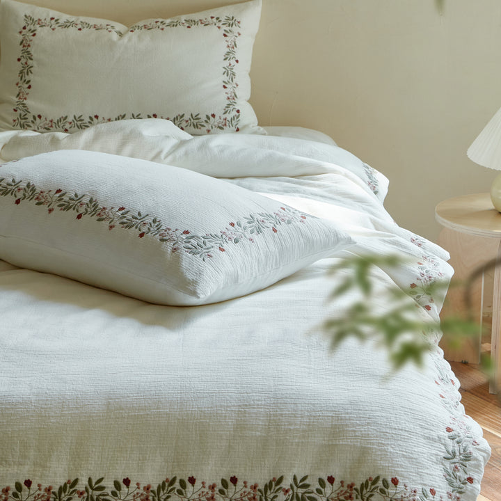 Rosebud Garland duvet cover and matching embroidered pillow shams arranged together on a white bed.