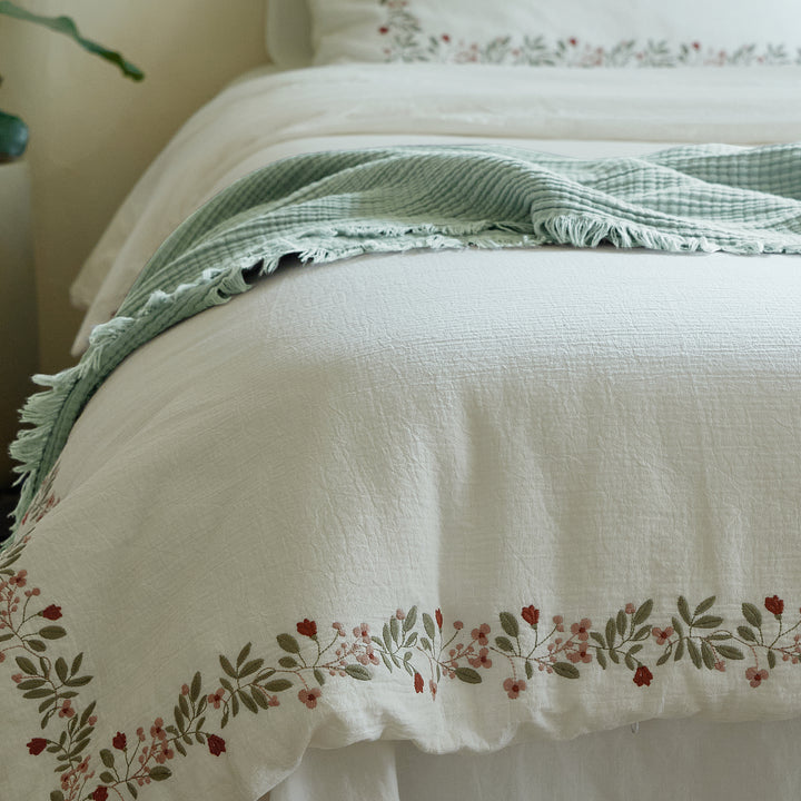 Rosebud Garland duvet cover shown from the foot of the bed with a sage green throw and embroidered border.