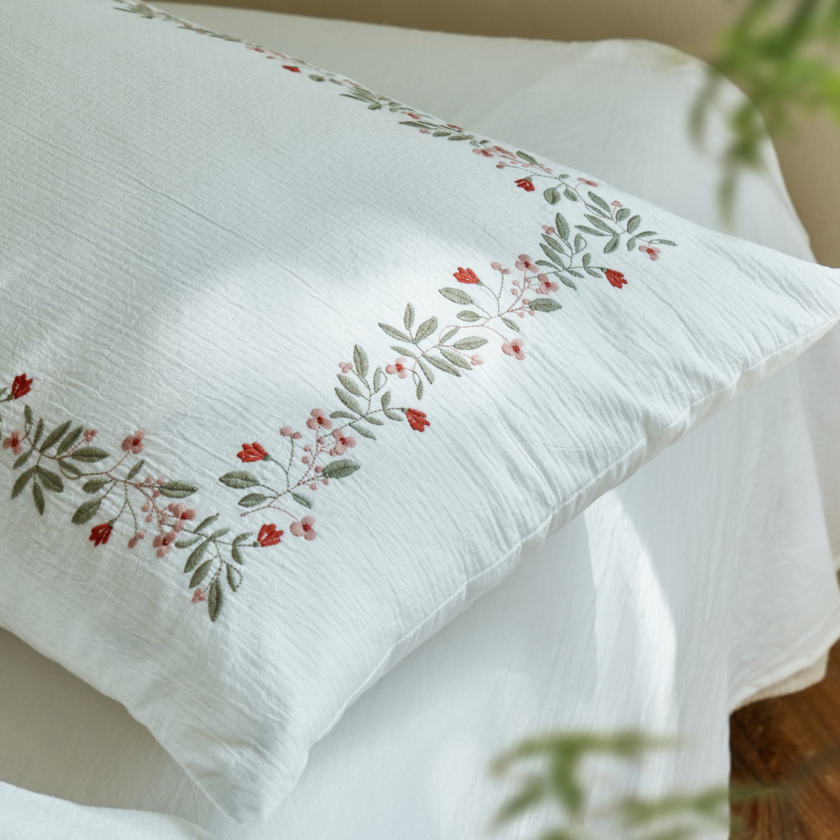 Close-up of a Rosebud Garland pillow sham featuring coral flowers, sage leaves, and raised botanical embroidery.