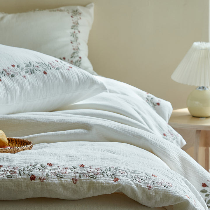 Side view of layered Rosebud Garland bedding showing the soft washed cotton drape and embroidered floral border.