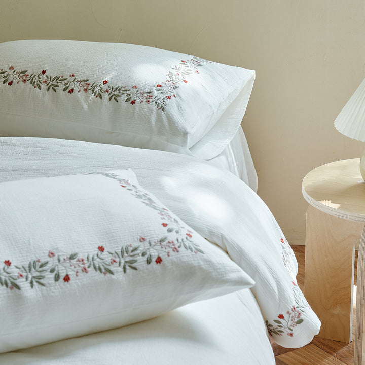Matching Rosebud Garland pillow shams with continuous coral and sage botanical embroidery.