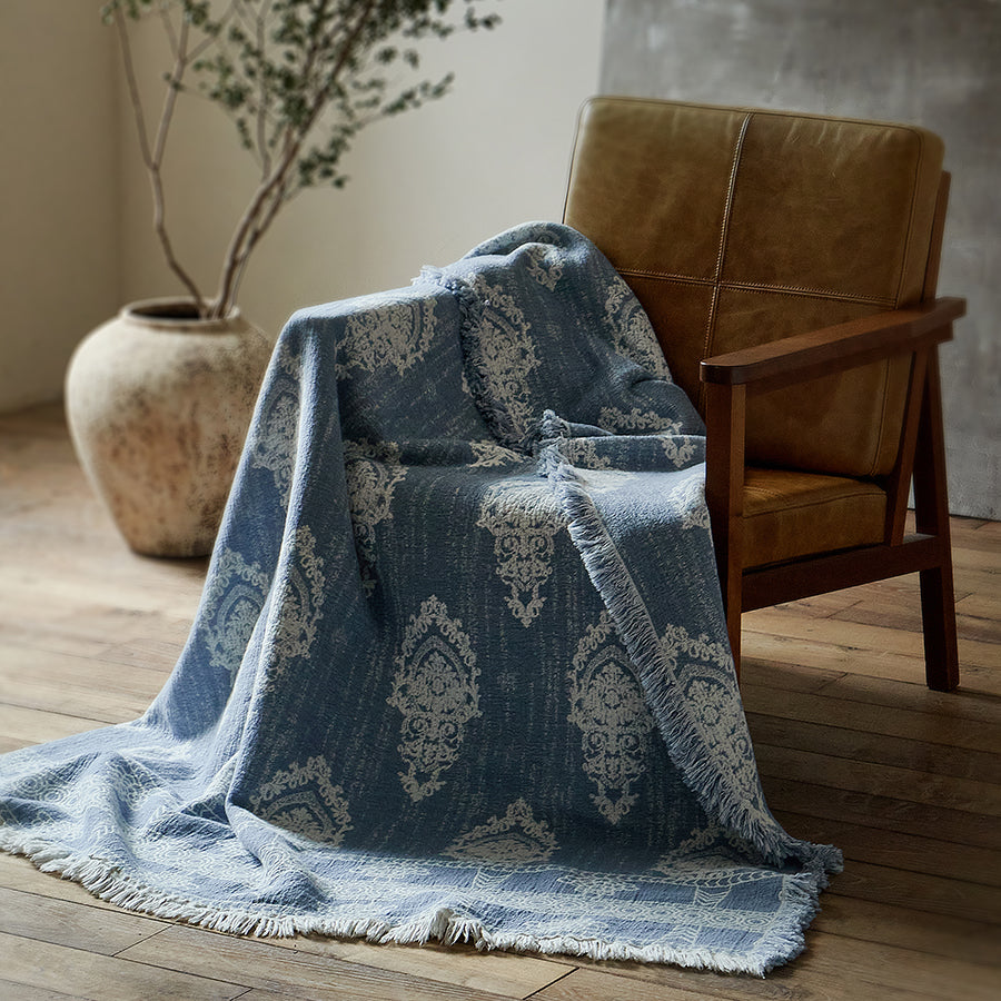 Dusty blue cotton-linen jacquard blanket draped casually over a wooden and leather armchair.