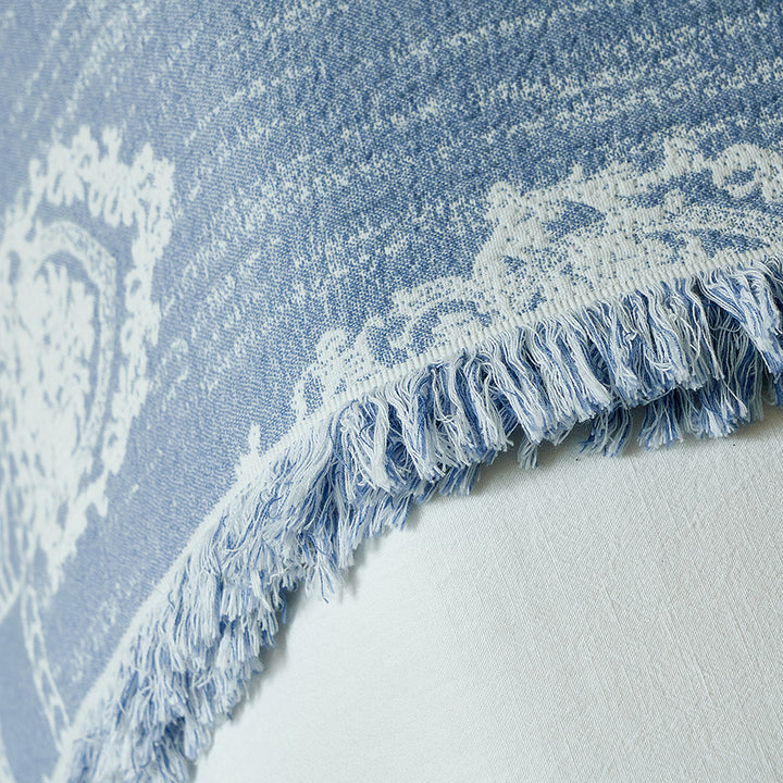 Dusty blue textured throw blanket draped over the edge of a bed, showing the elegant pattern.