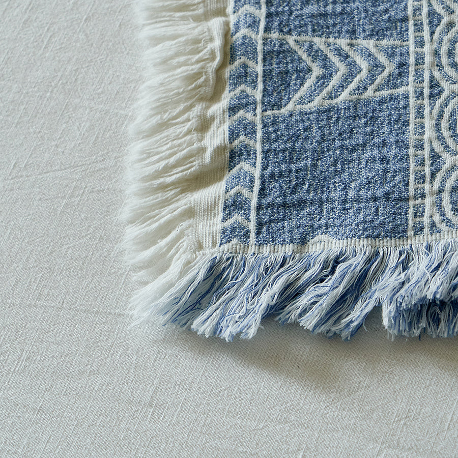 Macro shot of the fringe detailing and white geometric patterns on the dusty blue blanket.
