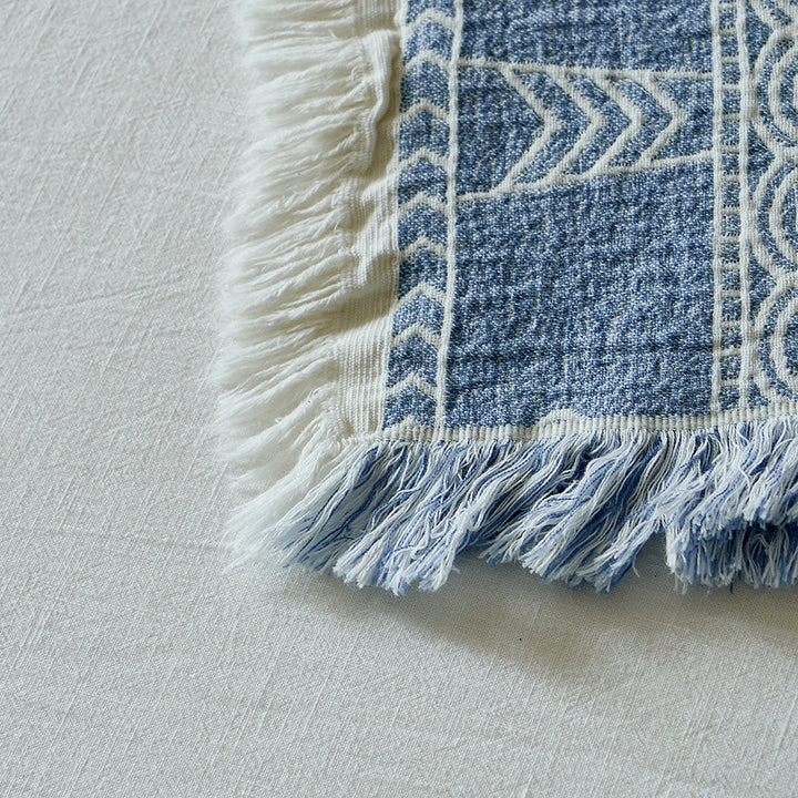 Macro shot of the fringe detailing and white geometric patterns on the dusty blue blanket.