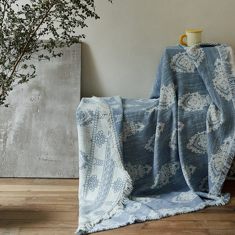 Dusty blue cotton-linen throw blanket gracefully draped over a chair against a neutral wall.