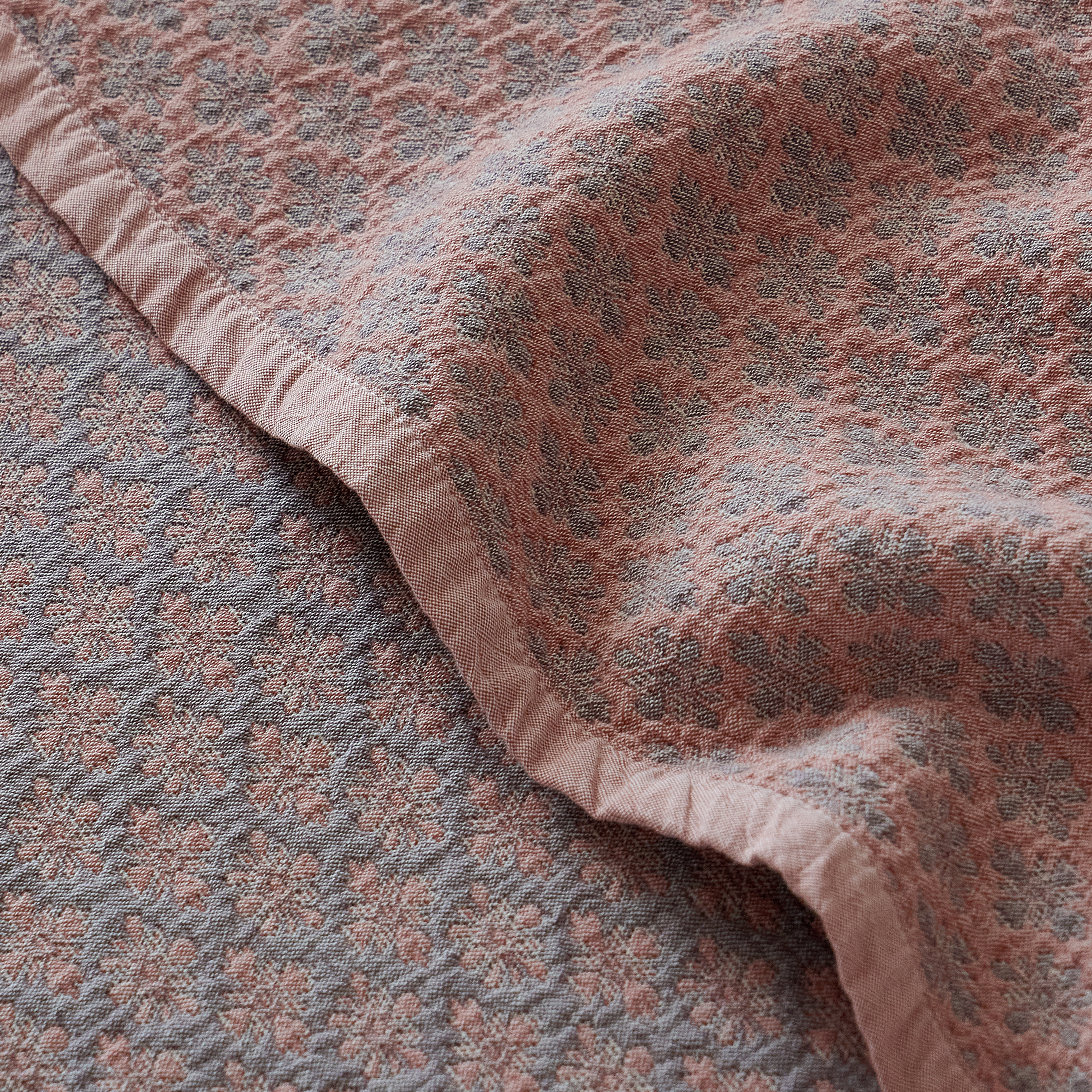 Folded edge of the dusty rose jacquard coverlet highlighting its heavyweight drape and woven texture.