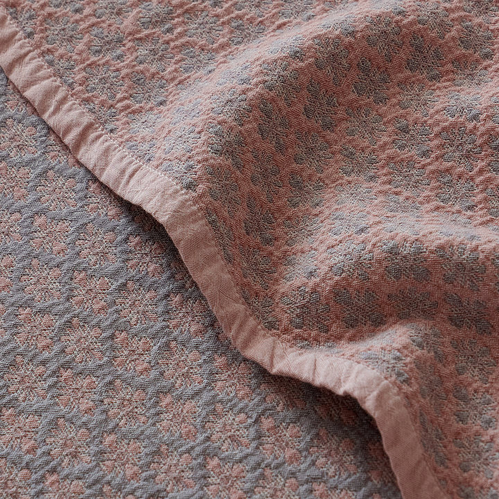Folded edge of the dusty rose jacquard coverlet highlighting its heavyweight drape and woven texture.