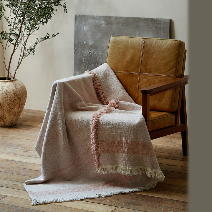 Dusty rose cotton-linen blanket draped casually over a brown leather armchair.